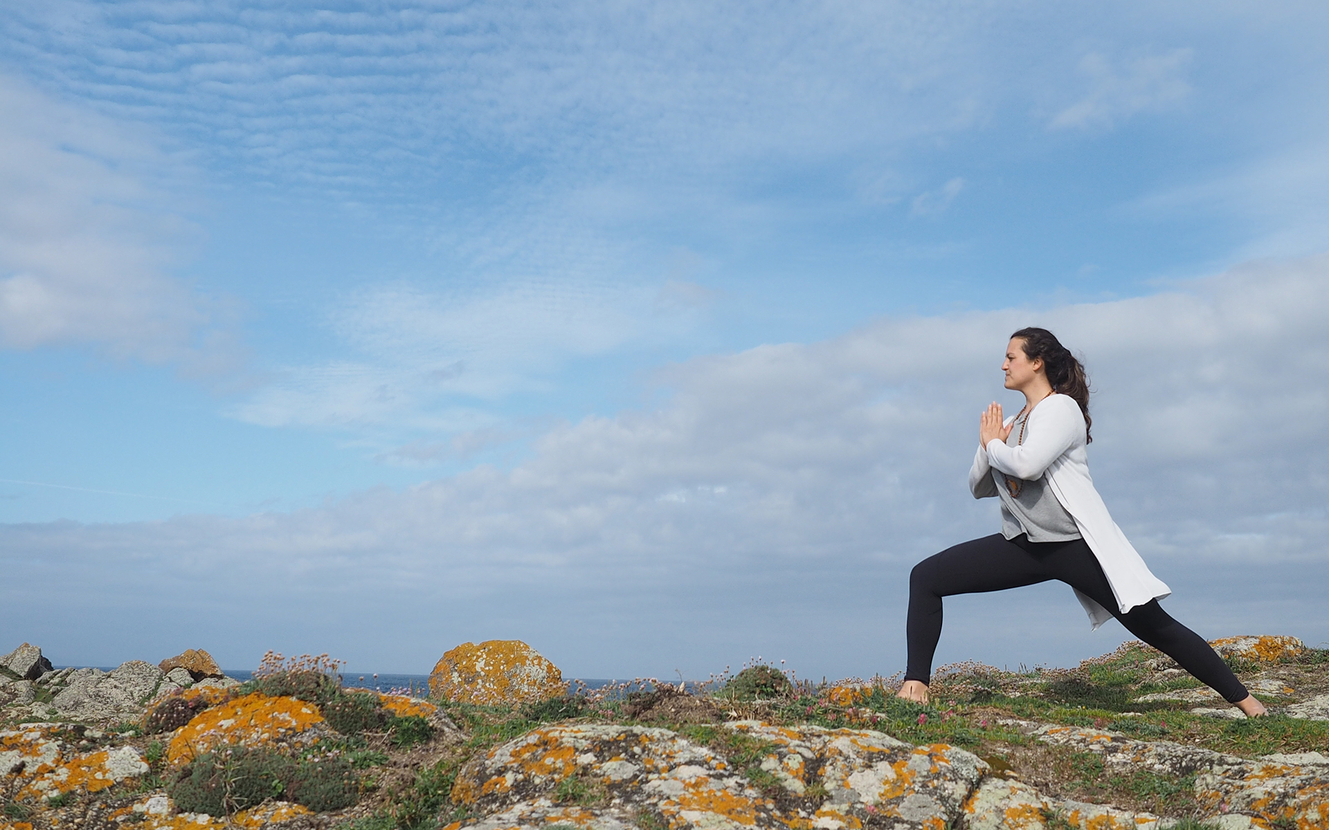 Mujer haciendo Yoga en una montaña con cielo azul y nubes. Aum Shala Yoga