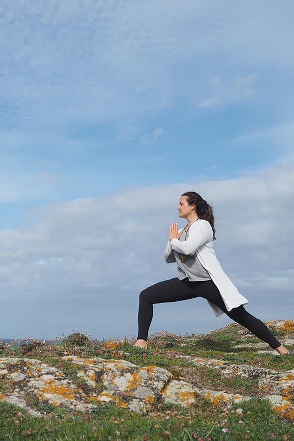 Mujer haciendo Yoga en una montaña con cielo azul y nubes. Aum Shala Yoga